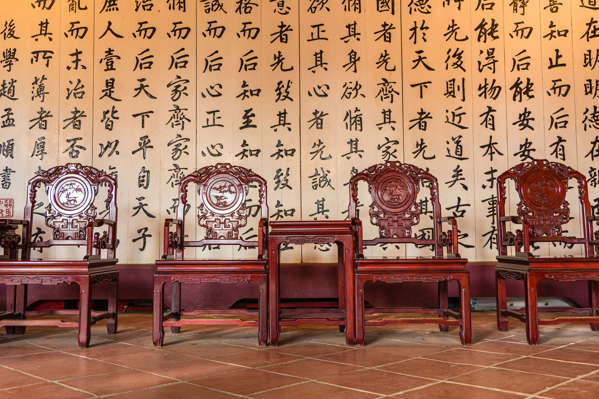 Chinese wood chairs arranged in front of calligraphy.