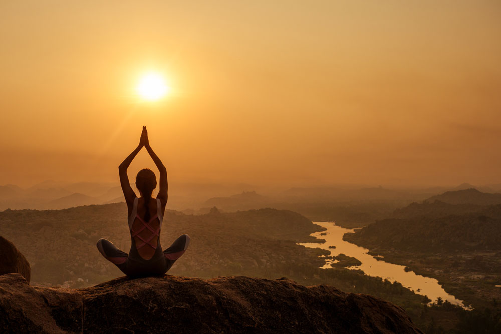 Yoga meditating at Hampi temple with the sun setting in the background.